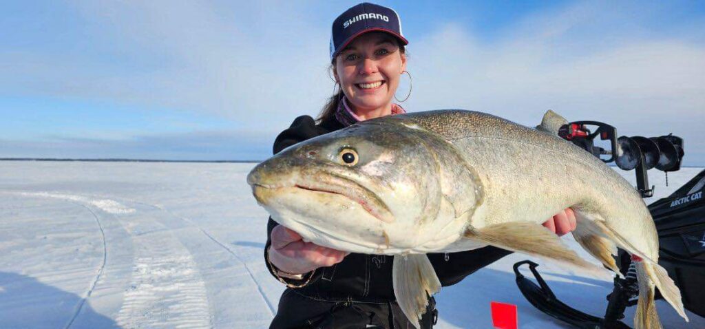Woman holding a big fish caught while ice fishing in the Canadian Shield