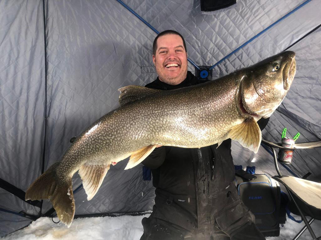 Happy man inside ice fishing tent holding a large fish