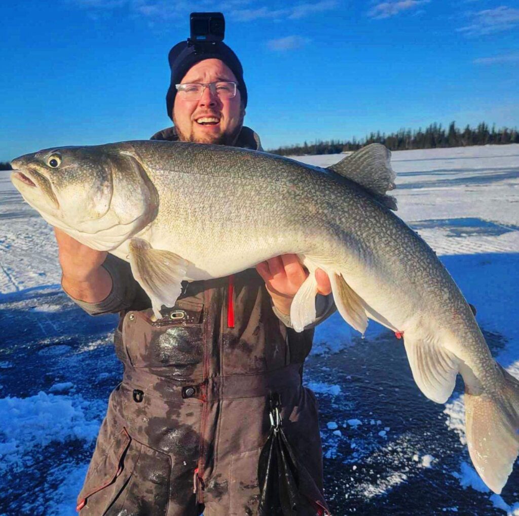Angler holding a trophy trout during a productive ice fishing day on Lake Athapapuskow.
