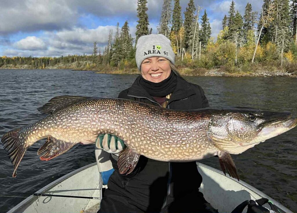 A woman holding a large fish on a boat, showcasing the scenic views at a premier Manitoba fishing lodge.