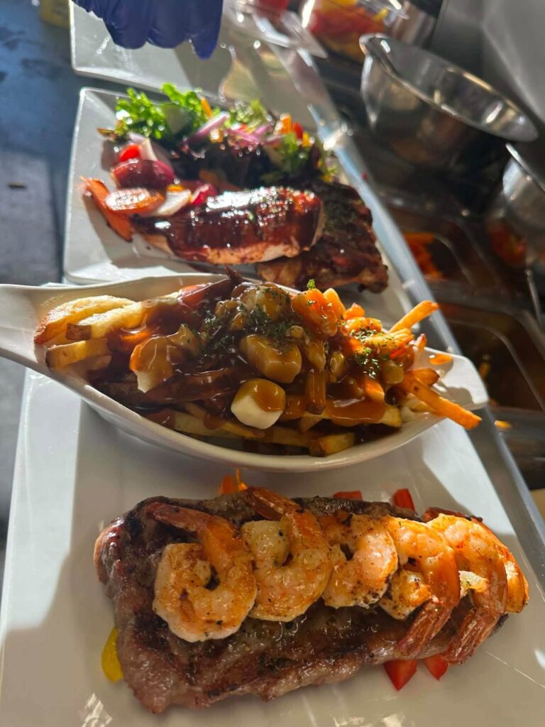 Grilled steak topped with shrimp alongside poutine and BBQ ribs from Bakers Narrows Lodge
