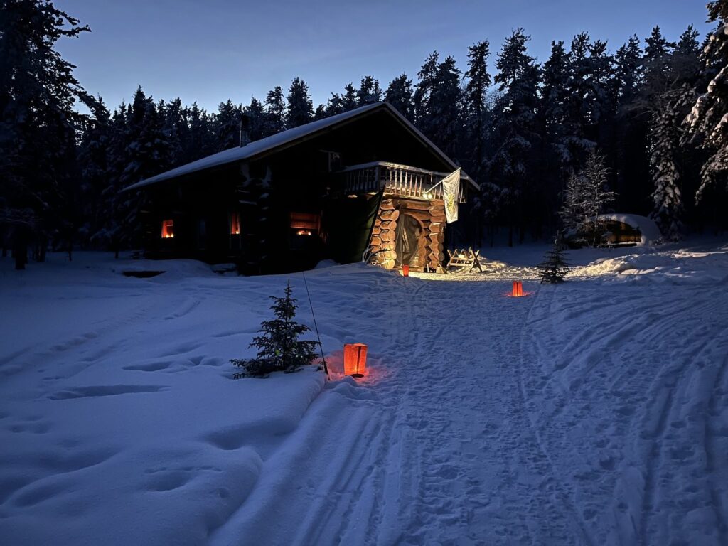 Kamuchawie Lake outpost lodge at dusk in winter with glowing lanterns in the snow