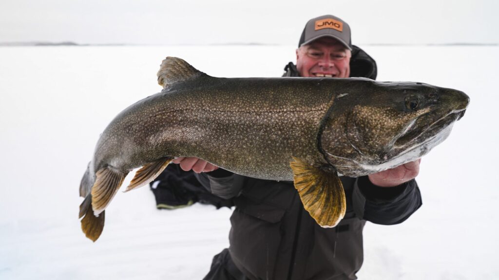 Angler holding a giant lake trout on the ice at Kamuchawie Lake